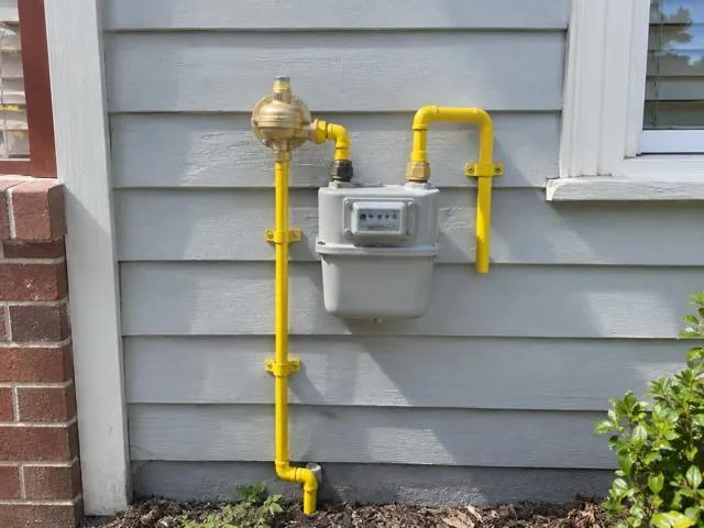 Exterior gas meter and yellow pipework on grey weatherboard wall in Maroubra